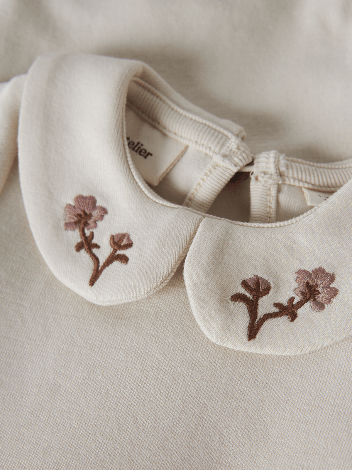 Nærbilde av krage med brodert blomst i rosa og brunt