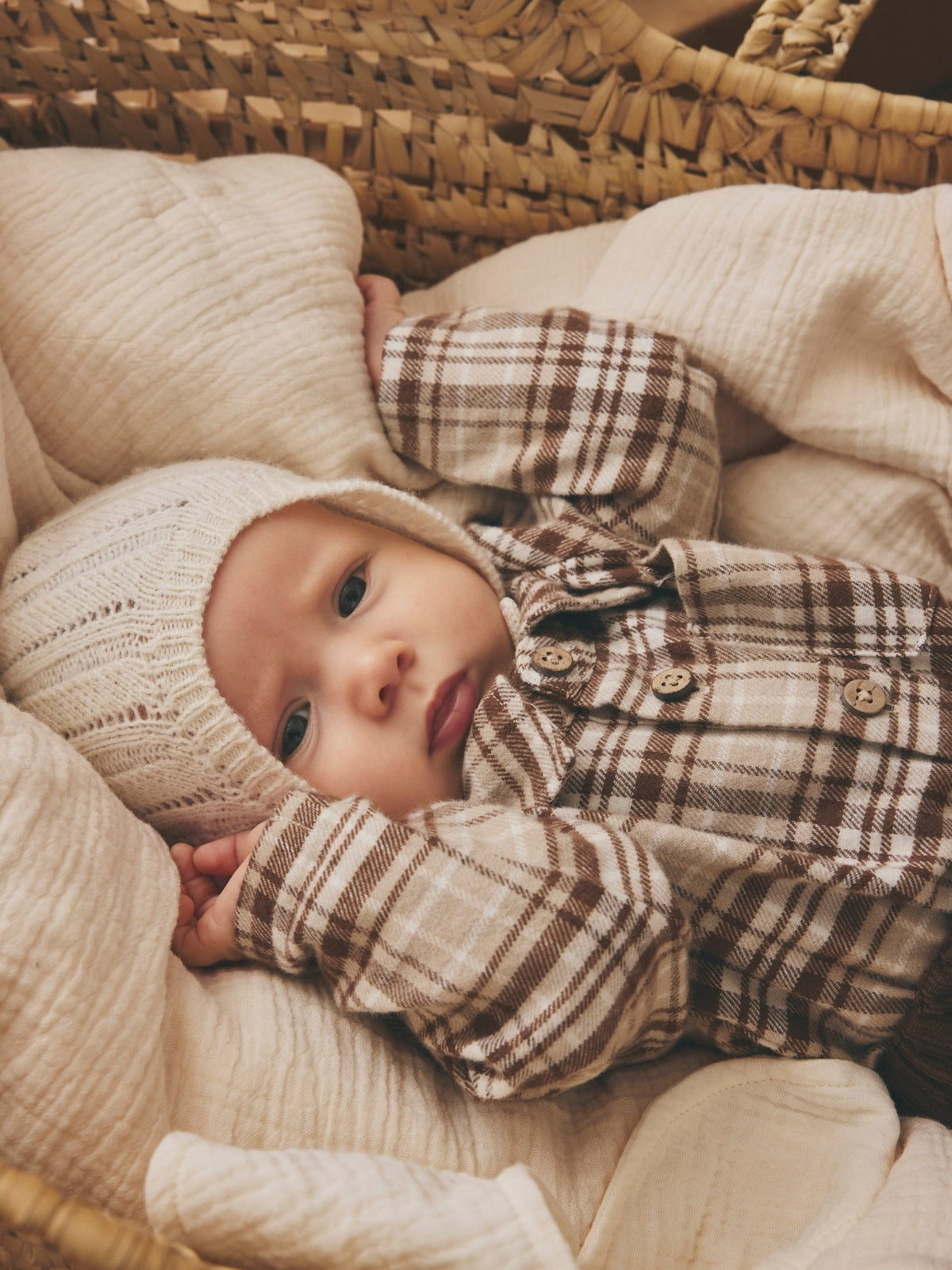 Baby i rutete skjortebody i beige og brunt som ligger i en kurv