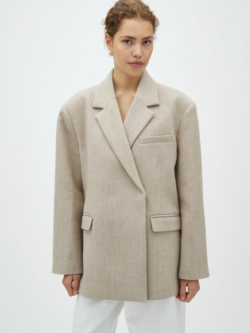 Modell i lys beige oversized blazer med hvite bukser, sett forfra